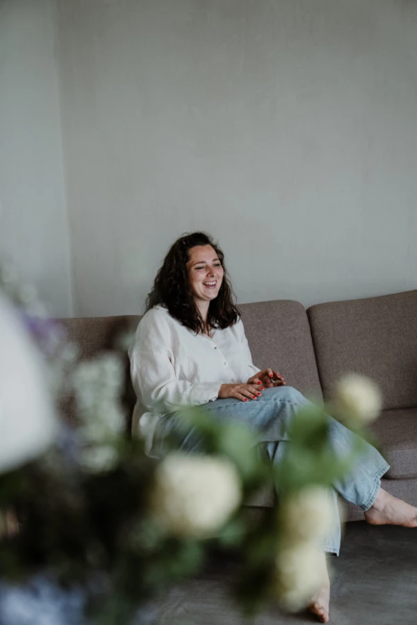 Hebamme Nina sitzt auf dem Sofa und lacht